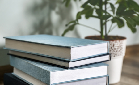 a stack of books next to a green plant